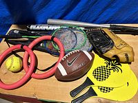 Photo of the sports equipment and balls showing bats, glove, rackets, ball, and rings.