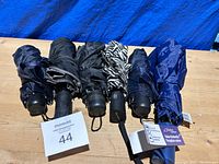 Photo showing six folded travel umbrellas aligned horizontally on a blue background, highlighting their compact size, handles with wrist straps, and variety of dark colors including a zebra striped pattern.