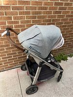 Three-quarter front view showing grey heathered canopy, seat fabric, silver frame and front swivel wheels.