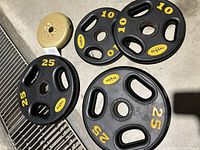 Photo showing two 25 lbs black weight plates and two 10 lbs black weight plates, all with yellow 'Fit 4 Less' markings and three hand grips each.
