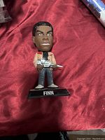 Front view of Finn bobble head holding a blaster with 'FINN' labeled base on red fabric background