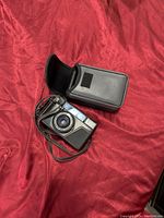 Full view of vintage Nikon camera with lens and carrying strap beside black protective case.