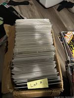 Photo showing a top view of a large quantity of comic books packed tightly in a worn cardboard box. Each comic is individually sleeved.