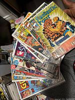 A hand holding a stack of various Marvel comic books including Fantastic Four, showing their front covers with colorful superheroes and dynamic action illustrations.