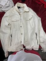 White denim jacket laid flat showing button and zipper-pocket details