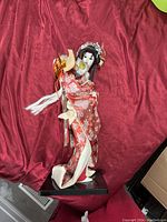 Side view of the handcrafted Japanese geisha figurine on a red fabric background highlighting the detailed kimono and accessories.