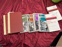 Multiple Shakespeare books laid out on red cloth including complete works volumes and individual plays