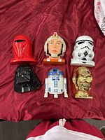 Set of six Star Wars character headset replicas arranged on red fabric background showing each helmet and droid detail