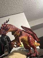 Large red and yellow dragon toy figurine posed on a surface, showing detailed scales, horns, wings, and claws.
