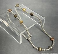 Close-up of the necklace draped over a clear display stand illustrating the multiple tiny silver beads and larger multicolor spherical beads.