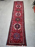 Top-down full view of red Persian runner on grey floor showing overall design and length