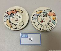 Two round pottery dishes with hand painted abstract faces in color and black lines, displayed side-by-side.