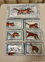 Top view of all seven ceramic pieces arranged on a table, showing the tiger hand paintings on the rectangular platter and six smaller dishes.