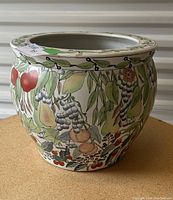 Rounded ceramic plant pot with detailed hand-painted fruit and leaves on a light background shown from one angle.