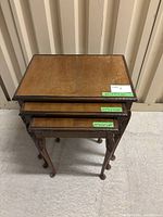Photo showing three nested carved wooden tables stacked and viewed from above, showcasing table tops and carved edges.
