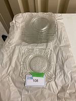 Stack of ten clear square Imperial Glass plates with floral daisy pattern visible on top plate.