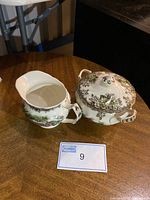 Two-piece set showing cream pitcher and covered sugar bowl with Friendly Village scenic village pattern in green and brown.