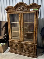 Full front view of the mid century wooden china cabinet with two glass doors and four bottom drawers. Hand carved detail visible at the top crown area.
