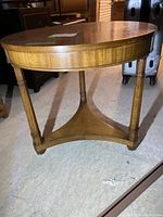 Full side view of round mahogany lamp table showing triangular lower shelf and three legs.