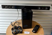 Samsung HW-E450 soundbar with six speaker drivers, a Samsung subwoofer PS-WE450, Logitech remote, three HDMI cables and one optical cable arranged on a tabletop.