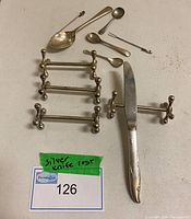 All items displayed on a tabletop including 4 silver cutter rests, 4 spoons of various sizes, 2 appetizer forks, and a silver knife.