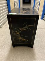 Side view showing bird and bamboo floral painted decoration on black lacquer wood cabinet.