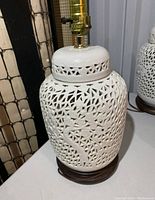 Overall view of the white ceramic Blanc De Chine lamp with intricate cut-out design on the body and the wooden base.