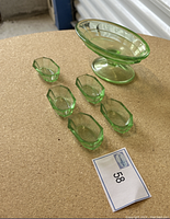 Overall view of the vintage green glass footed banana split bowl with the five small matching green bowls arranged on a tabletop.