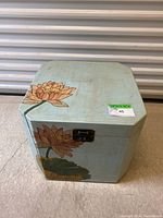 Front angle view of vintage hinged cube coffee table with floral lotus painted decoration and metal latch on lid.