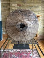 Front view of the antique wooden wagon wheel on a metal stand against a brick wall and wooden furniture background.