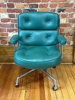 Front view of turquoise green leather chair showing button tufted seat and backrest against brick background