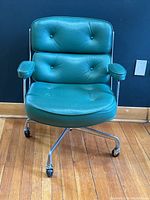 Front view of chair showing turquoise leather button-tufted back and seat with padded armrests and five-star castered base