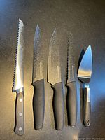 Full set of five cutting utensils arranged side by side on a dark surface, showing variety in blade shapes and handle styles.