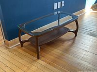 Overall angled view of the rectangular glass top coffee table with curved faux walnut legs and lower shelf, emphasizing design and condition.
