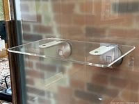 Clear side view of the modern wall-mounted acrylic shelf attached to frosted glass/smooth surface with two suction cup mounts.