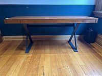 Full front view of desk showing narrow wood surface and steel trestle legs