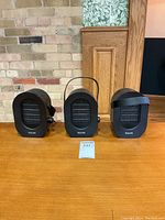 Three black Hisome portable ceramic space heaters on wooden surface, showing front view and size comparison.
