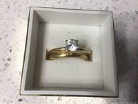 Top-down view of wedding ring set in a small white box showing both rings stacked together, solitaire ring on top.