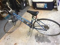 Side angle showing full blue frame, black saddle, and front drop handlebars of the Schwinn ladies bike with visible wear and missing tires.