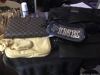 Overview of five purses included in the lot: brown checkered wallet on top of beige handbag, black PINK brand fabric bag, smooth black purse, and textured dark gray purse.