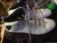 Side view of pair of white Air Jordan Take Flight sneakers with black and red accents, showing shoe details and profile