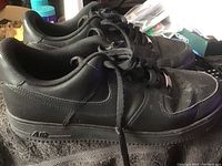 Side view of black Nike Airforce 1 men's sneakers showing leather upper, perforated toe box, and midsole air branding.