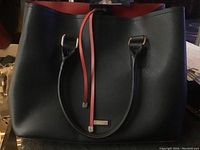 Front view of the black purse with dual handles and red strap detail.