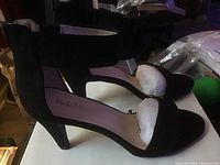 Side view of black high-heeled shoe showing ankle strap and heel