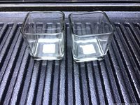 Two clear square glass containers placed side by side on a black surface, showing their transparent and clean condition.