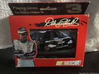 Front view of the red collector tin box containing two decks of Dale Earnhardt playing cards, showing NASCAR branded race car through window, Dale Earnhardt's image and autograph.