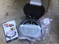 Opened meal maker shown with three compartments inside, accompanied by original box and manual on outdoor surface.