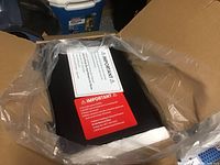 Photo of a black Honeywell safe still in plastic wrap inside an open cardboard box, showing warning labels on the safe's front.