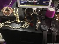 Full lot showing jewelry, three watches, sunglasses, and portable speaker on black surface