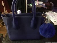 Front view of purple ladies purse with handles and fluffy purple pom-pom charm attached